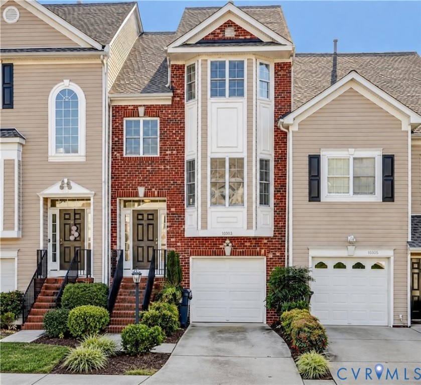 Multi-level facade featuring red brick masonry and horizontal siding, a central bay window, arched window detailing, and individual concrete driveways with attached garage bays Multi-level facade featuring red brick masonry and horizontal siding, a central bay window, arched window detailing, and individual concrete driveways with attached garage bays