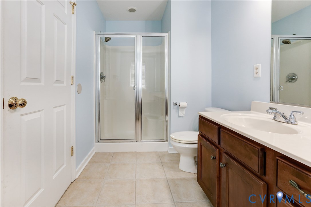 Bathroom featuring tile flooring, a dark wood vanity with a solid surface countertop, an integrated sink with a chrome faucet, and a glass-enclosed shower