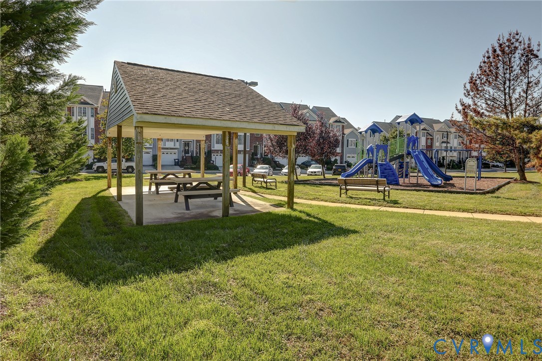 Community common area featuring a covered pavilion, playground equipment, manicured lawn, and paved walkways