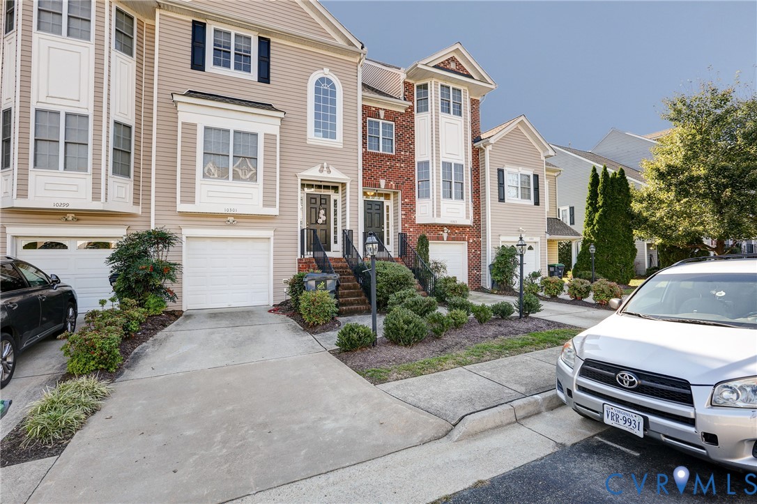 Multi-story townhome exterior featuring vinyl siding, brick accents, arched window detailing, and an attached single-car garage