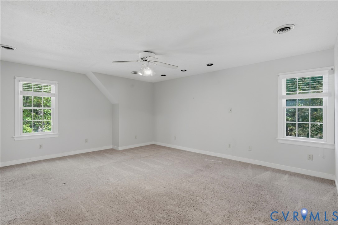 Neutral-toned interior space featuring carpeting, recessed lighting, a ceiling fan with integrated lighting, and multiple windows with white trim