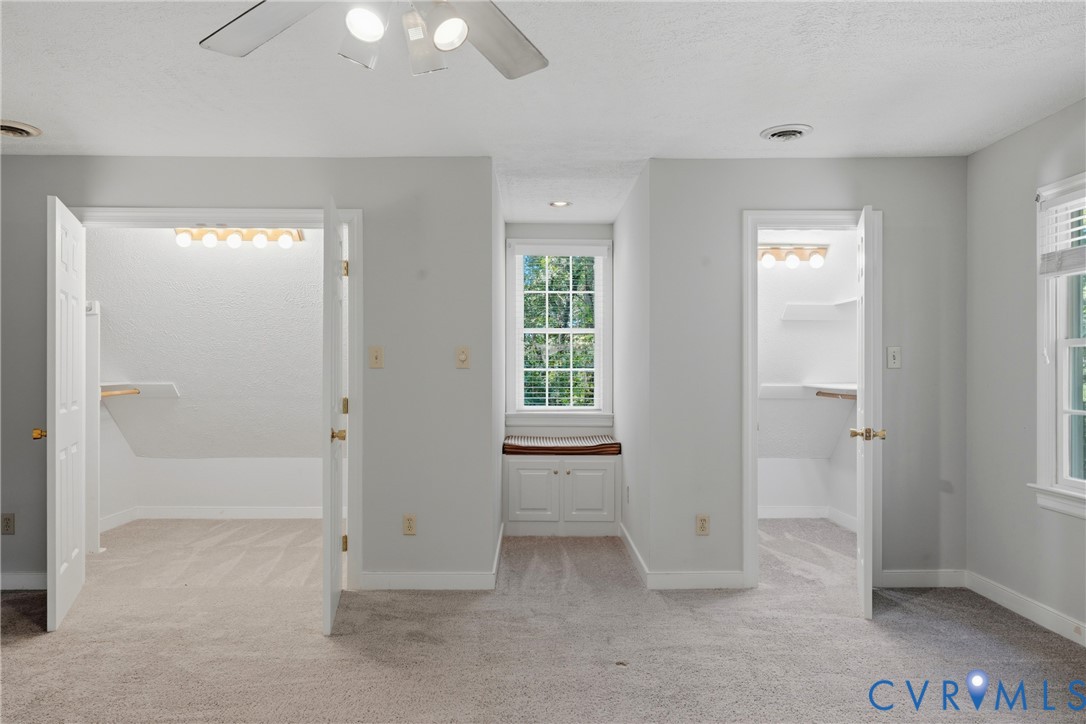 Carpeted room featuring dual reach-in closets, a recessed window nook with built-in cabinetry, and a ceiling fan with light kit