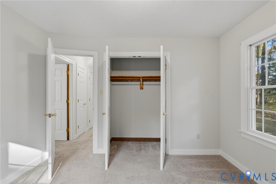 Interior space featuring neutral-toned carpeting, a built-in reach-in closet with overhead shelving, multi-panel doors, and a double-hung window with muntin detailing