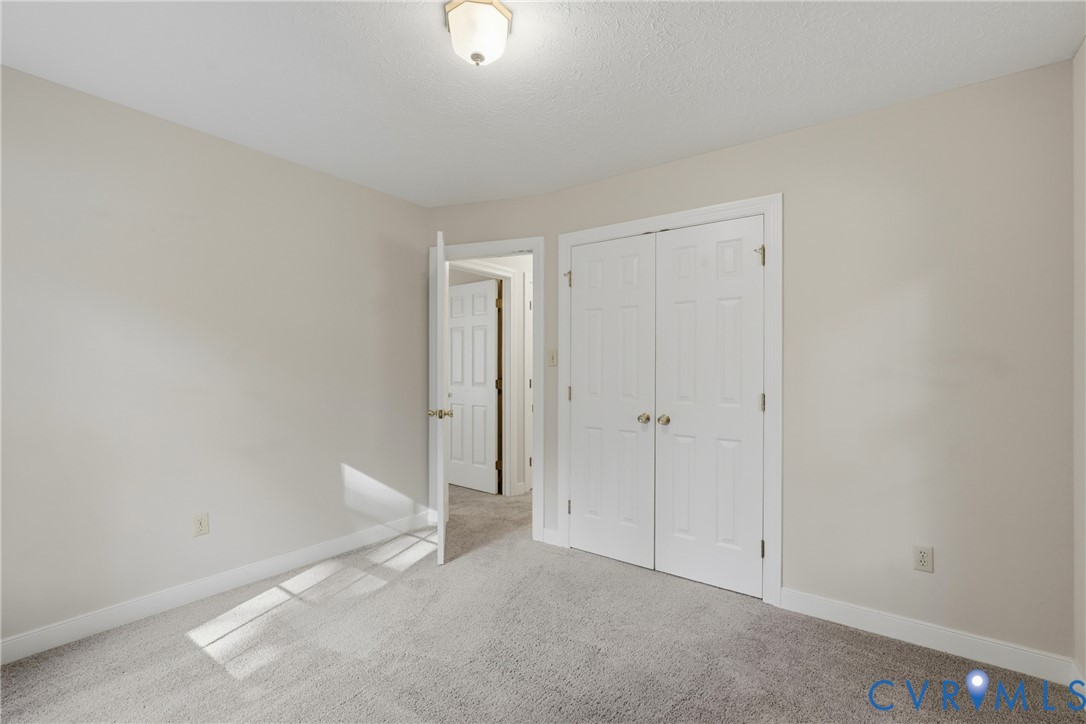 Neutral-toned interior room featuring wall-to-wall carpeting, a double-door closet with six-panel doors, and a central overhead ceiling light fixture
