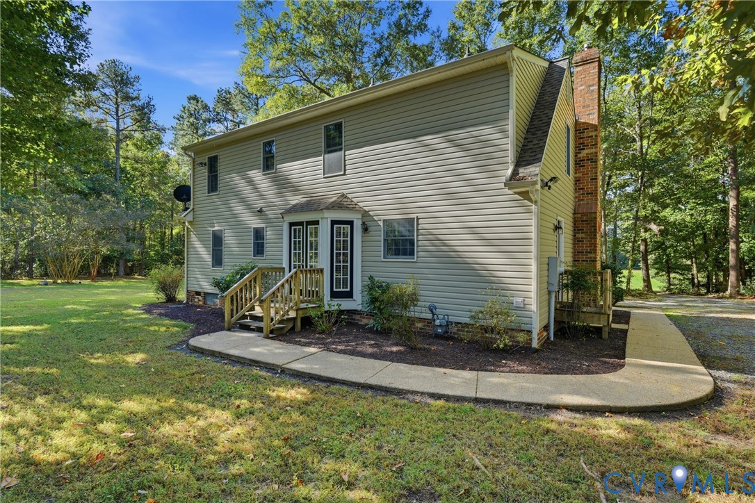 Two-story exterior featuring light-colored horizontal siding, a prominent brick chimney, multi-pane glass entry doors, wooden steps, and a curved concrete walkway