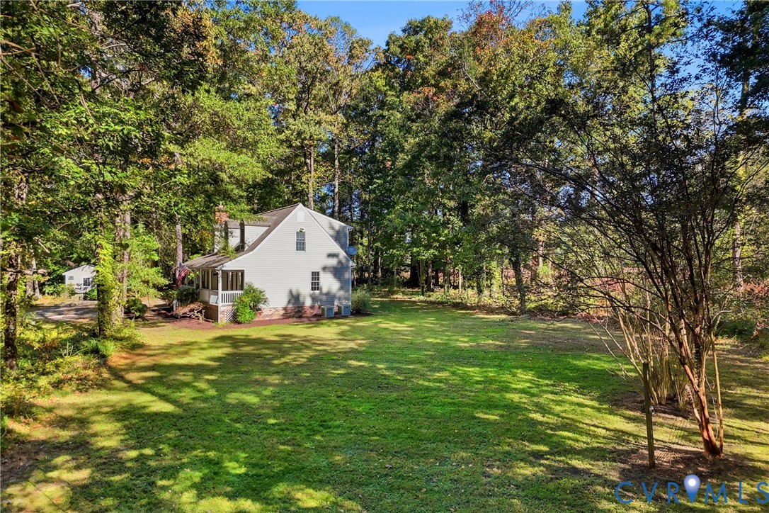 Expansive backyard featuring a level lawn, mature trees, and a residential structure with a covered porch and brick foundation