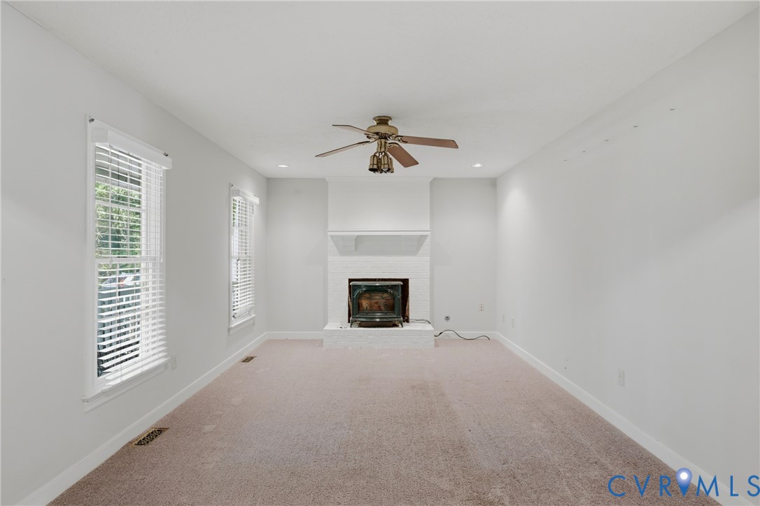 Neutral-toned interior featuring a white-painted brick fireplace with a wood-burning insert, carpeting, recessed lighting, and a ceiling fan with integrated light fixtures