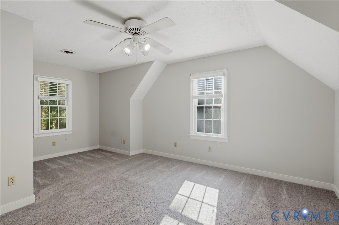 Interior room featuring wall-to-wall carpeting, vaulted ceilings, multi-pane windows, and a ceiling fan with integrated lighting