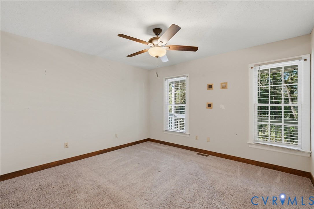 Neutral-toned interior space featuring wall-to-wall carpeting, wood-finish trim, dual double-hung windows, and a central ceiling fan with integrated lighting