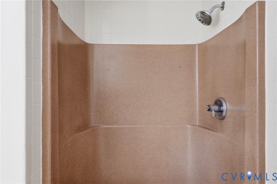 Shower stall featuring a molded composite surround, white tile wall accents, and a brushed metallic shower head and mixing valve