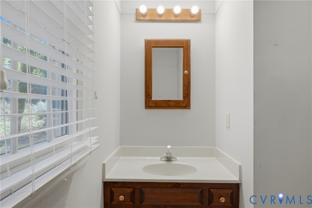 Bathroom featuring a wood-finish vanity with a built-in basin, coordinating wall-mounted medicine cabinet, four-light vanity fixture, and horizontal window blinds