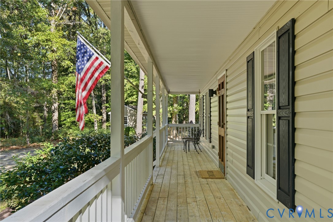 Covered porch featuring light-toned wood flooring, white railings, siding exterior, and black window shutters