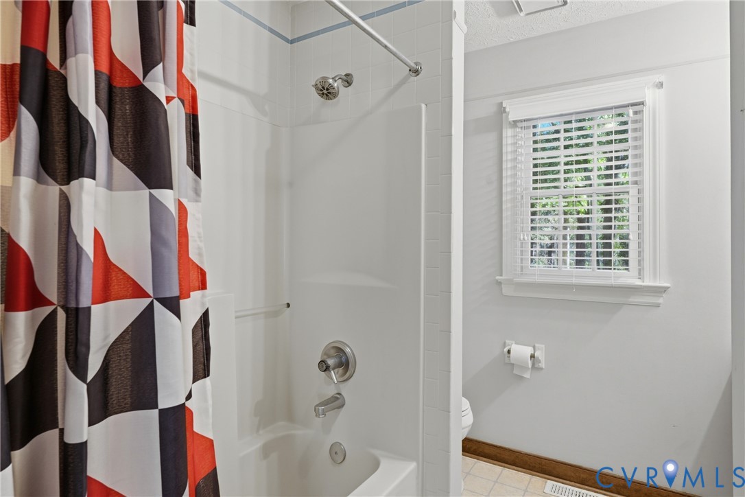 Shower and bathtub combination featuring white wall surround, chrome fixtures, and a window with white horizontal blinds