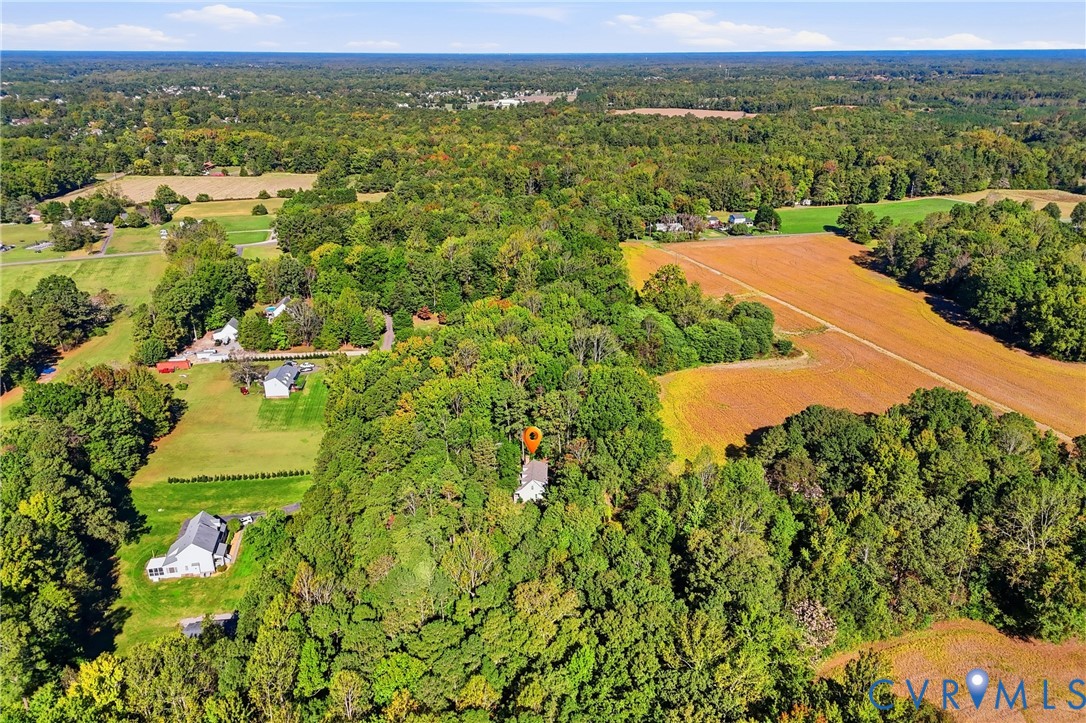Aerial perspective featuring a multi-story residence surrounded by dense woodland, mature trees, and expansive open fields
