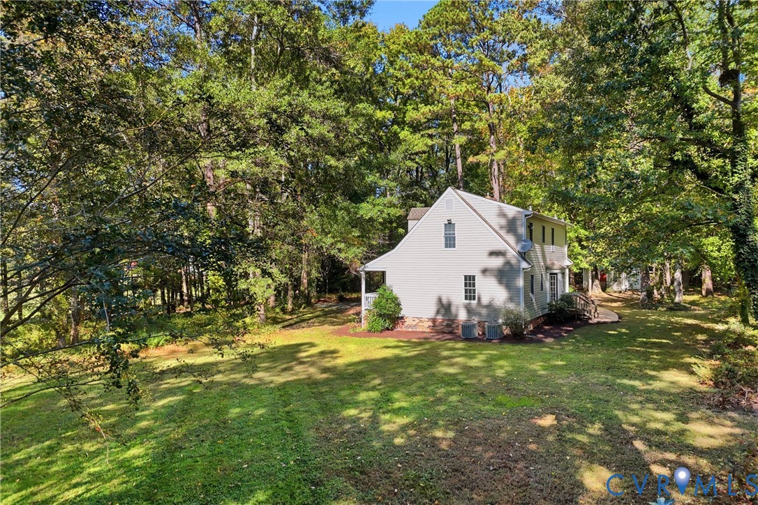 Two-story residence with light-colored siding, brick foundation detail, expansive lawn, and mature canopy trees