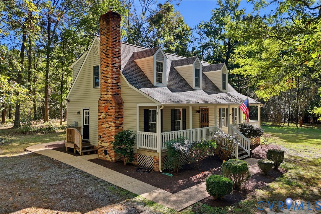 Two-story residence featuring light-toned horizontal siding, a prominent brick chimney, multiple dormer windows, and a covered front porch with railings Two-story residence featuring light-toned horizontal siding, a prominent brick chimney, multiple dormer windows, and a covered front porch with railings
