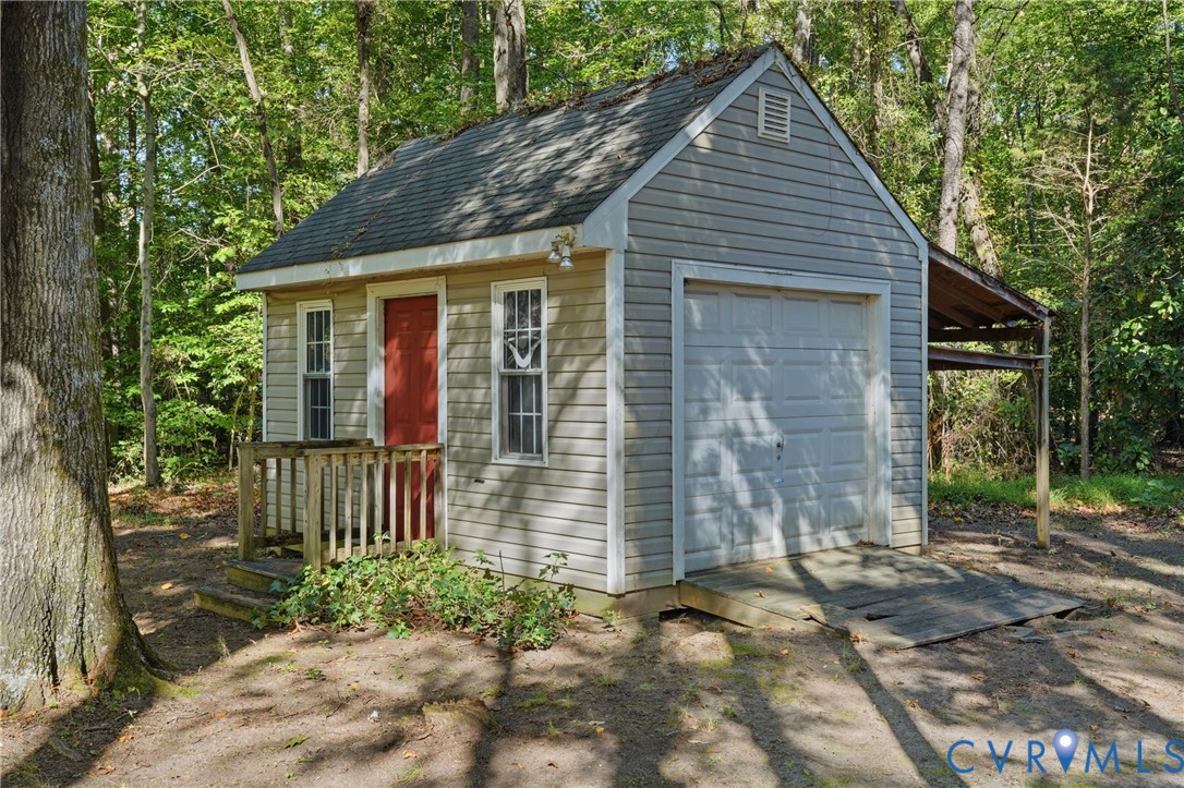 Detached structure featuring light-colored horizontal siding, a gabled asphalt-shingled roof, a sectional garage door, a side-hinged entry door, and a covered lean-to area