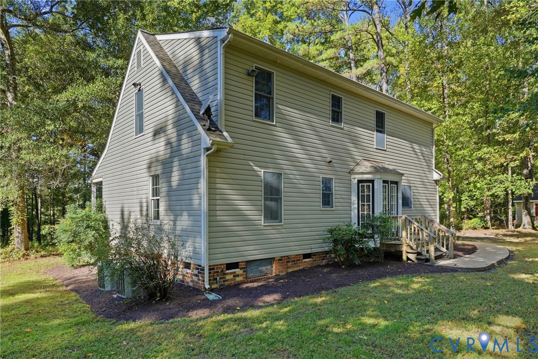 Two-story home with vinyl siding, gambrel roofline, raised rear deck, and masonry foundation base, situated on a wooded lot