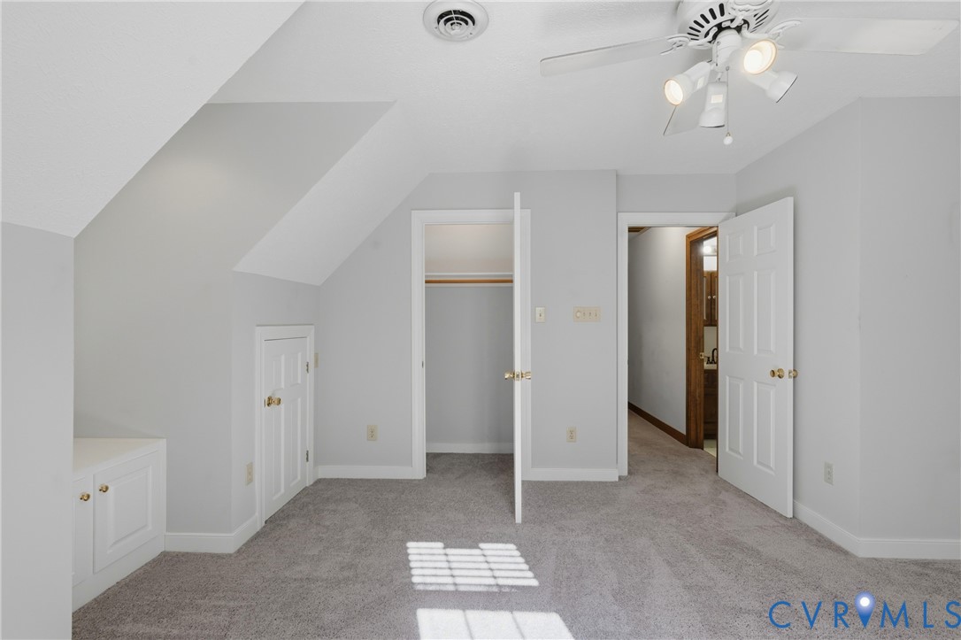 Neutral-toned bedroom featuring slanted ceilings, built-in cabinetry, walk-in closet, and a multi-bulb ceiling fan with integrated lighting