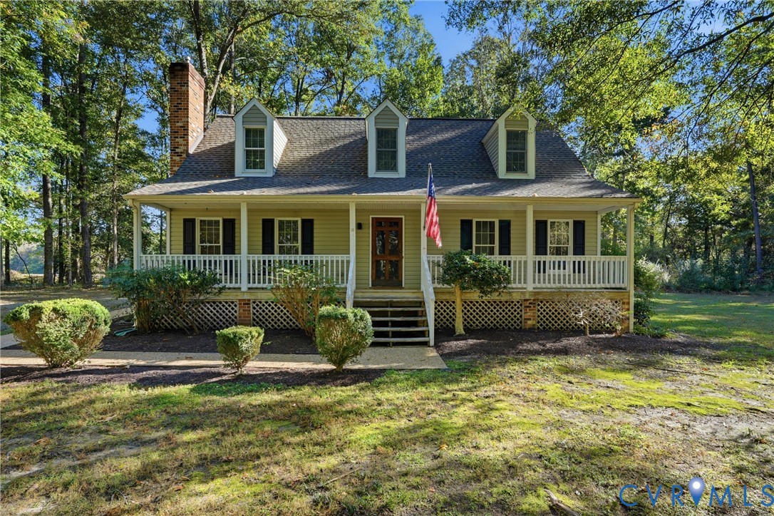 Cape Cod-style residence featuring a full-width covered front porch, brick exterior chimney, three dormer windows, and white lattice skirting