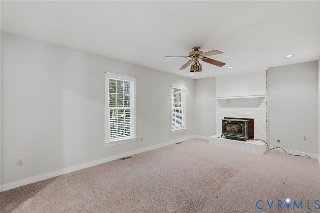 Brick fireplace featuring a hearth and integrated wood stove, double-hung windows, recessed lighting, and a ceiling fan