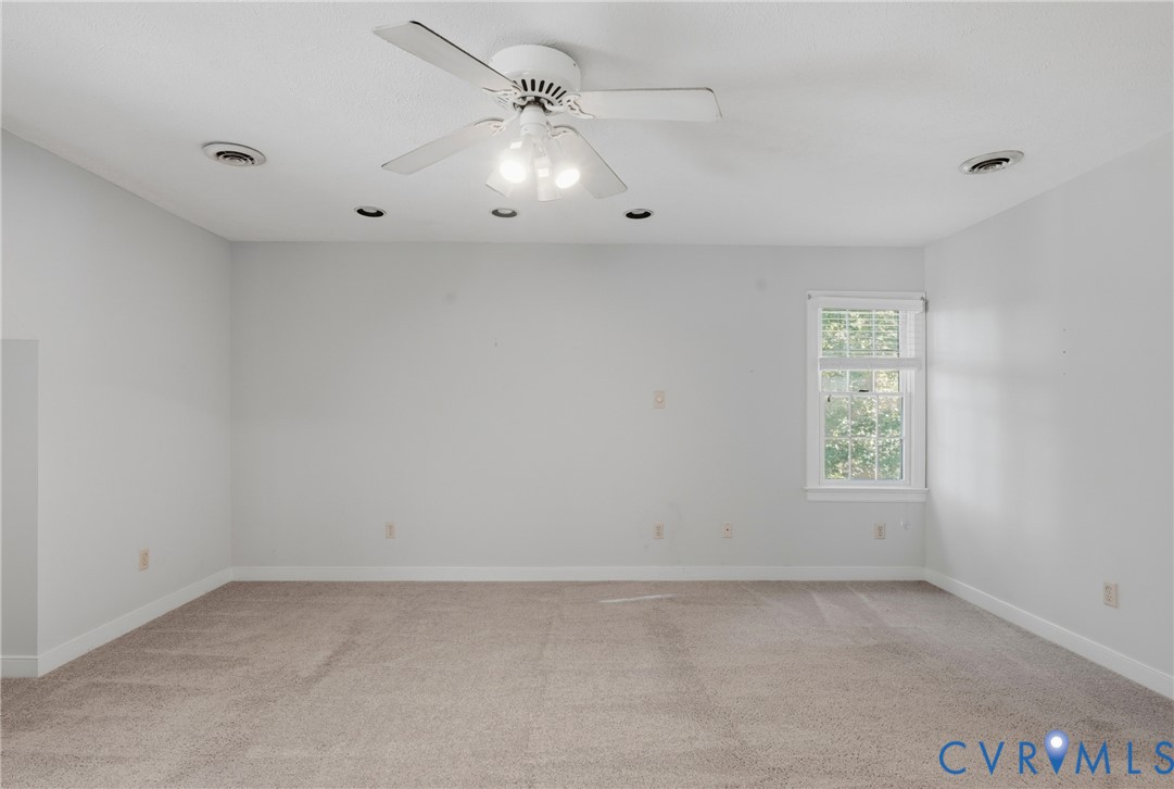 Neutral-toned interior space featuring wall-to-wall carpeting, recessed lighting, a white ceiling fan with integrated light fixture, and a single window with muntin detailing