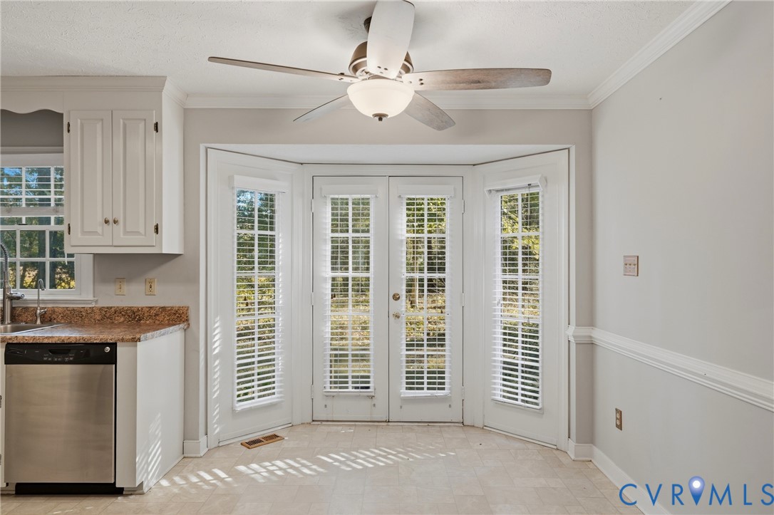 Dual French doors with pane glass panels, bay configuration, ceiling fan with integrated lighting, neutral wall palette, and built-in white cabinetry with stone-finish countertops