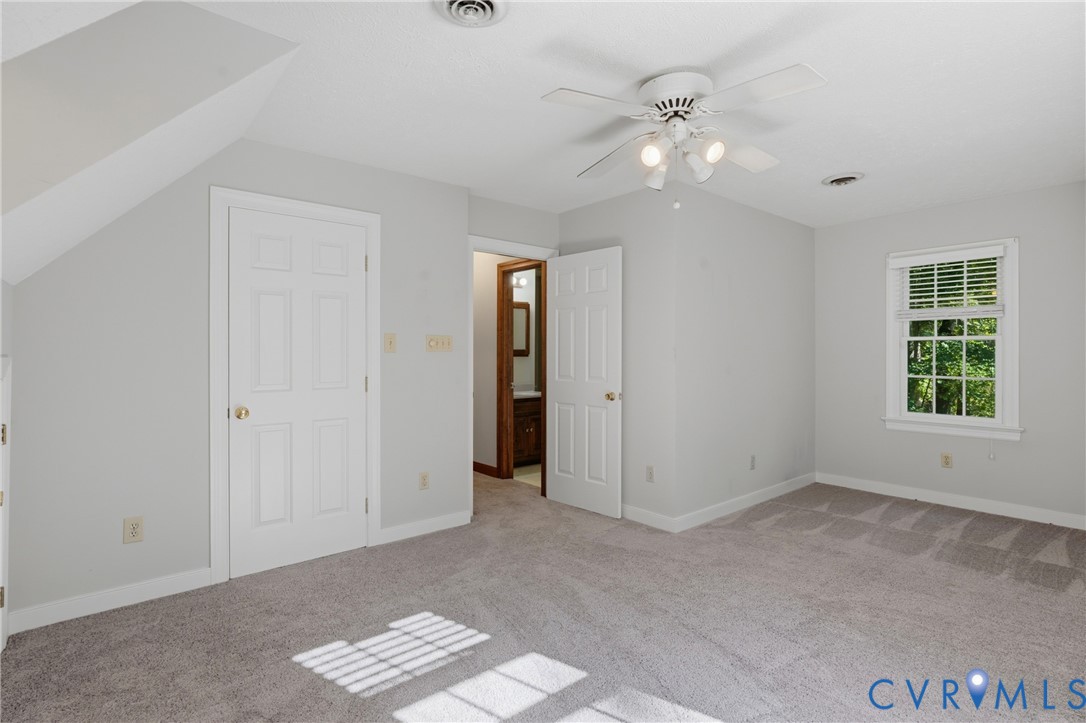 Neutral-toned room with plush carpeting, ceiling fan with integrated lighting, multi-pane window with grid inserts, and six-panel interior doors