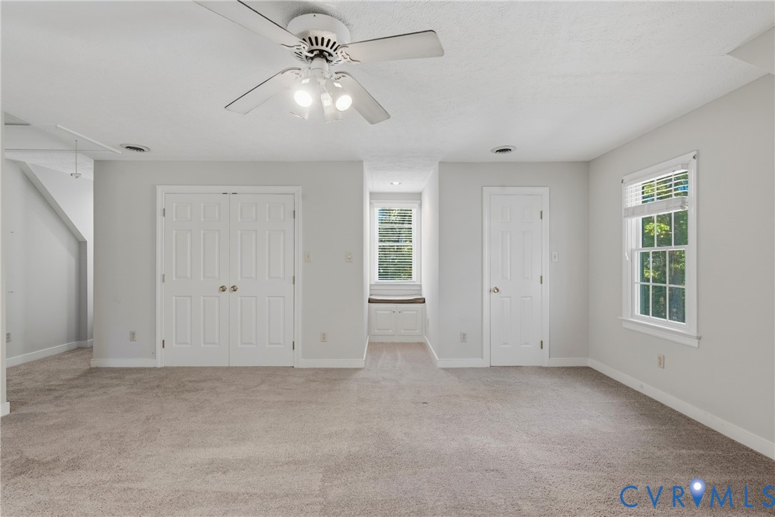 Room featuring carpeted flooring, a ceiling fan with integrated lighting, dual-panel closet doors, a single-panel interior door, and a built-in window seat with under-bench cabinetry
