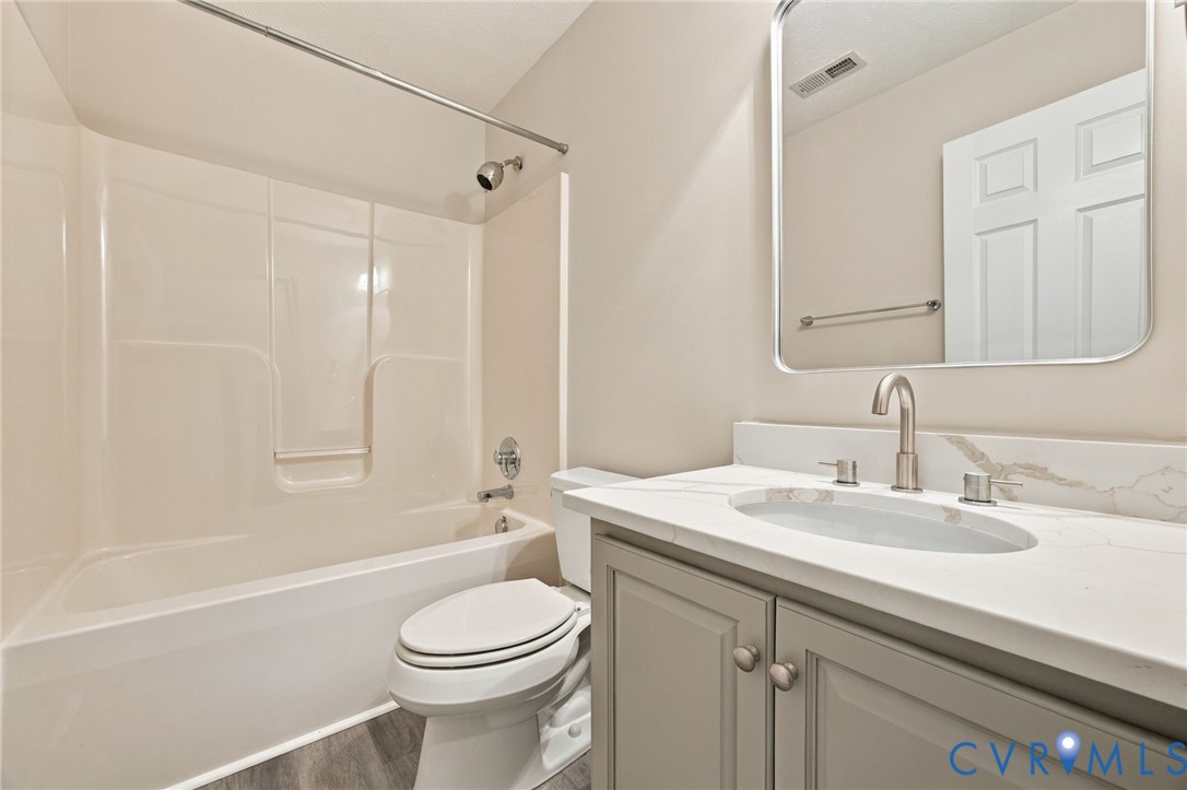 Bathroom featuring a vanity with grey cabinetry, a white countertop with integrated sink, brushed nickel faucet, rounded rectangular mirror, and a tub-shower combination with a surround