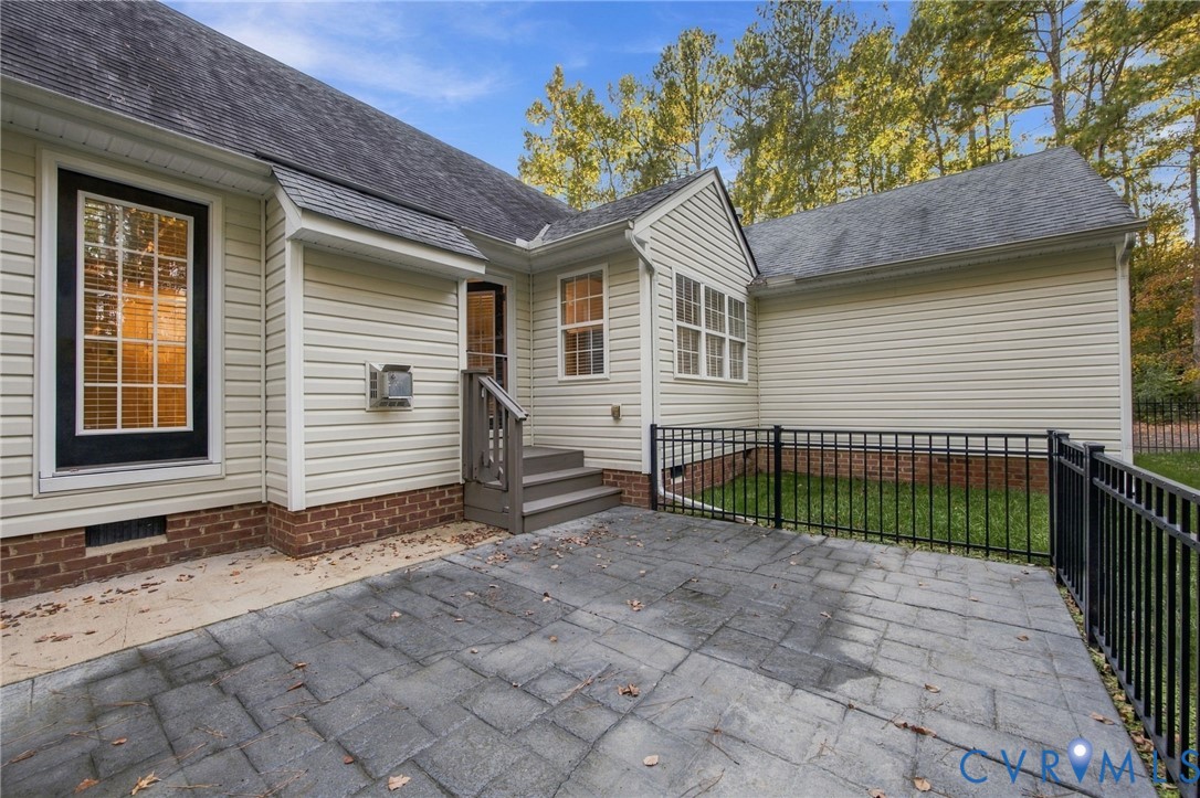 Rear exterior featuring a stone-finish patio, metal perimeter fencing, vinyl siding, and a brick foundation base