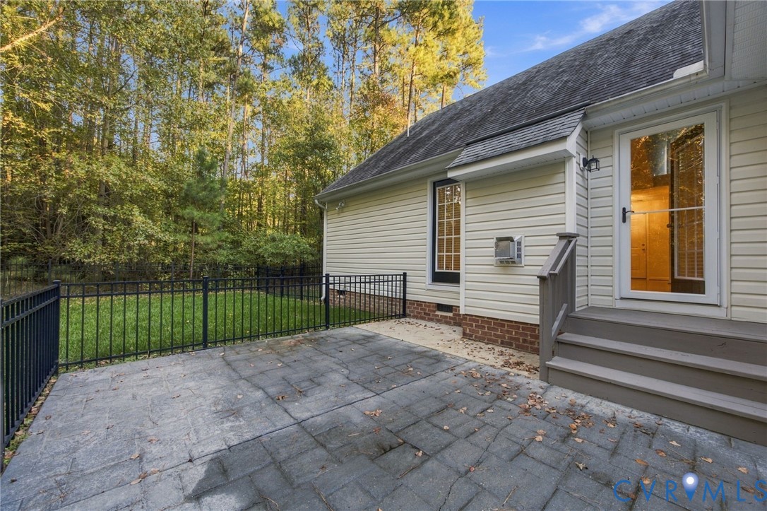 Rear exterior featuring a stamped concrete patio, black metal fencing, brick foundation accents, and a staircase leading to a glass-paneled door