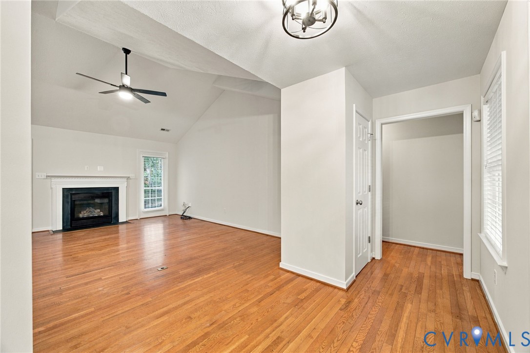Vaulted ceilings, wood-finish flooring, recessed fireplace with a mantel, ceiling fan, and overhead pendant lighting