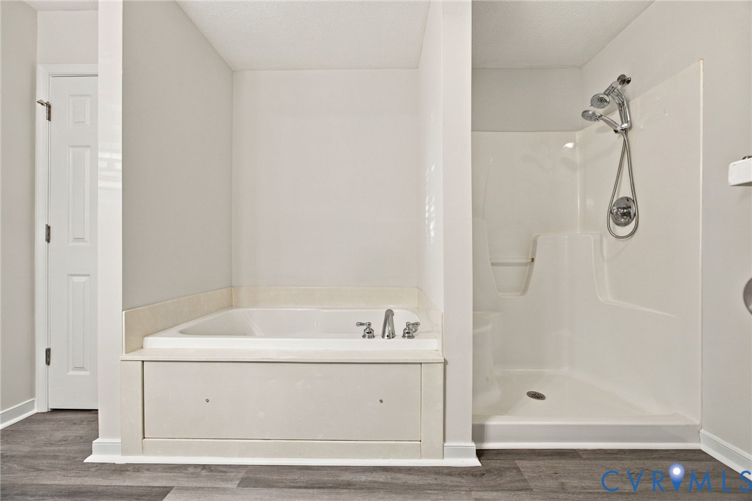 Soaking tub with a tile surround, separate stall shower with molded acrylic surround, adjustable handheld shower fixture, and wood-finish flooring