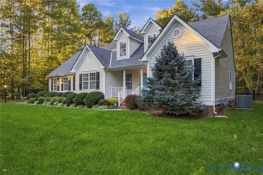 Traditional-style residence featuring horizontal siding, a gabled roofline with multiple dormers, a covered front porch with a white railing, and decorative window shutters, set against a backdrop of mature trees