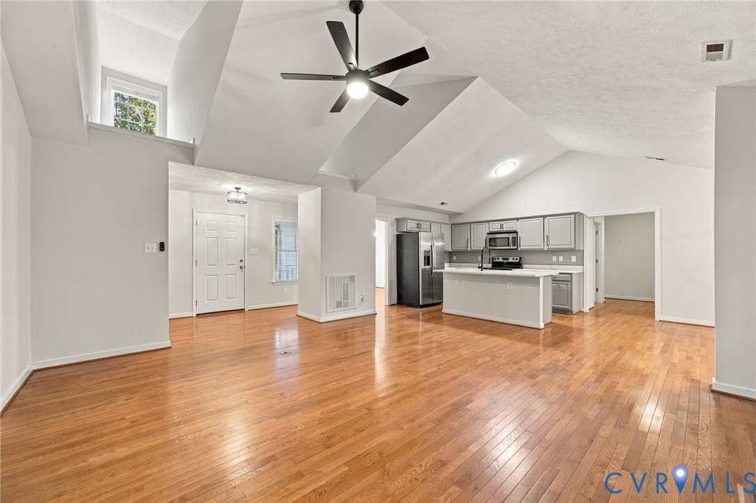 Vaulted ceilings, wood-finish flooring, kitchen island with countertop, and overhead ceiling fan