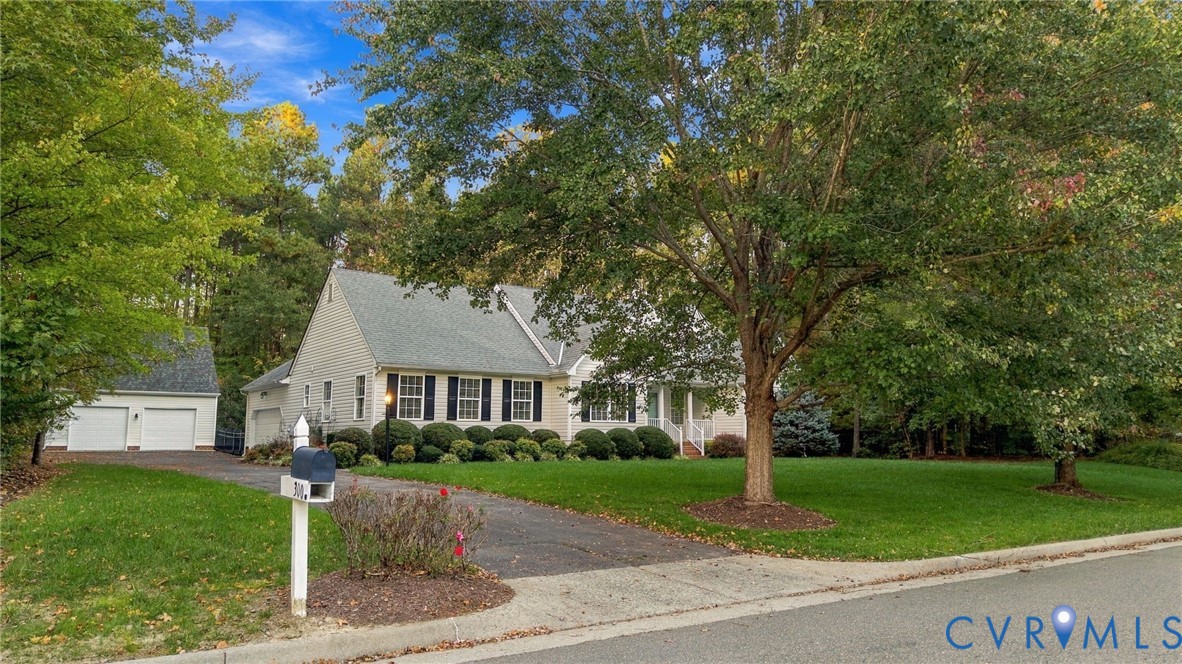 Cape Cod style exterior with light-colored siding, dark shutters, an attached two-car garage, mature landscaping, and a paved driveway