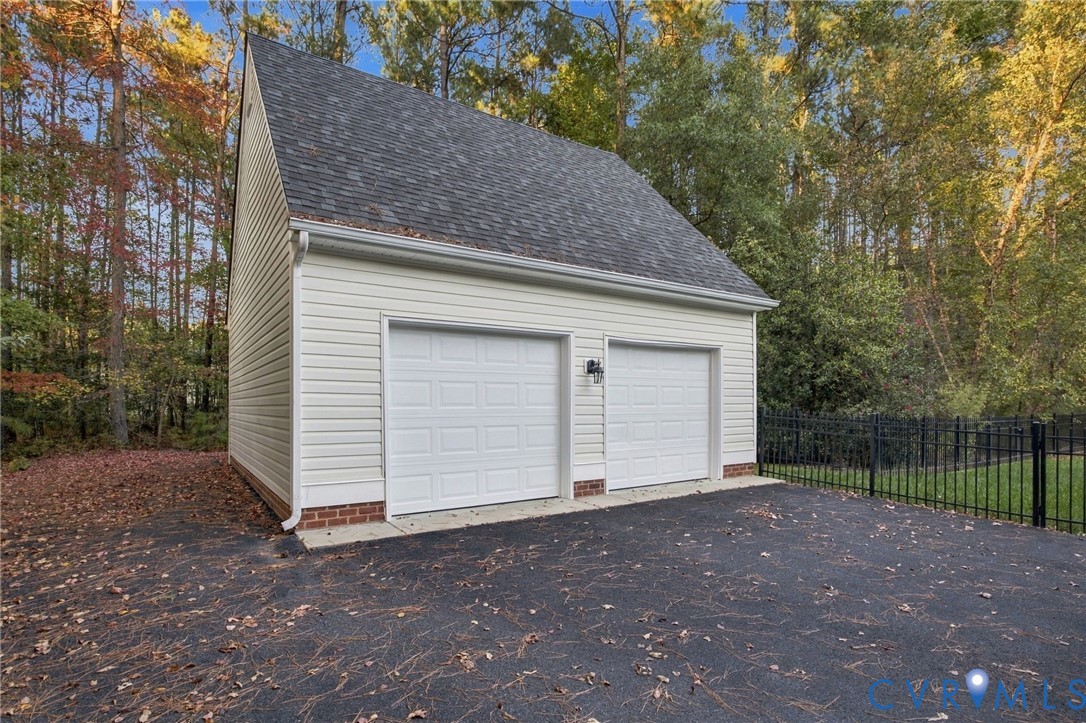 Detached two-car garage featuring light-colored horizontal siding, brick foundation accents, an asphalt shingle roof, and dual overhead doors