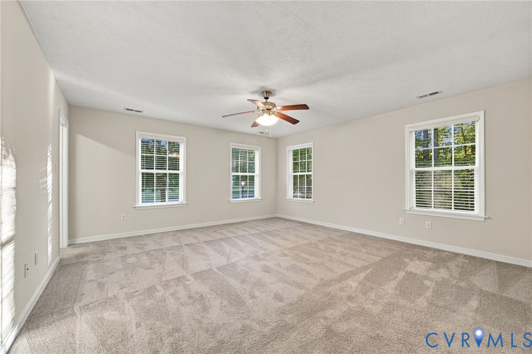 Neutral wall palette with plush carpeting, multiple multi-pane windows, and a central ceiling fan with integrated light fixture