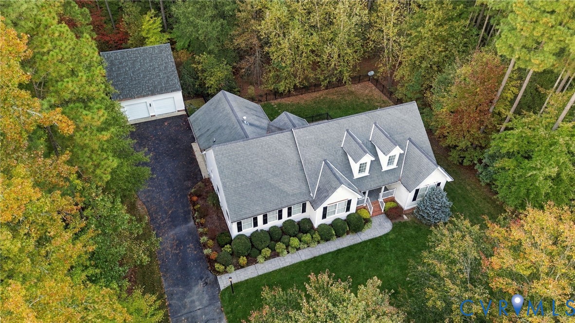 Aerial perspective of a multi-gabled residence featuring a detached two-car garage, asphalt driveway, asphalt shingle roofing, and manicured landscaping