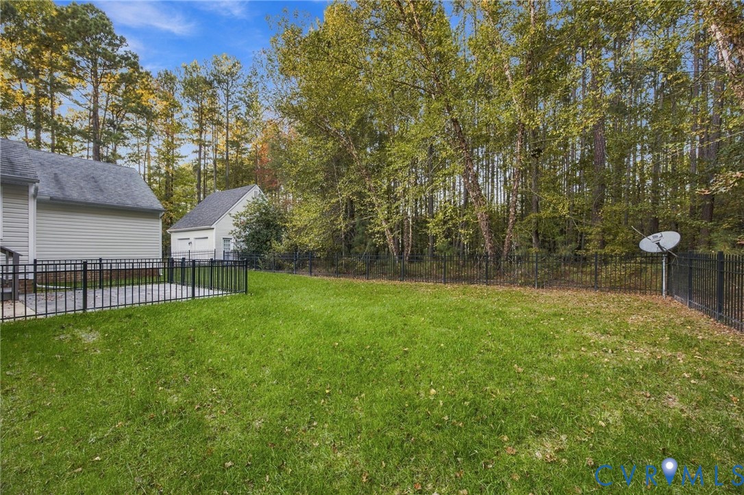 Rear yard featuring a paved patio, metal perimeter fencing, and mature trees