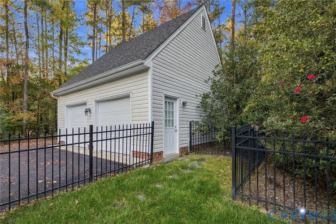 Detached two-car garage featuring light-colored horizontal siding, asphalt shingle roofing, brick foundation accents, and metal perimeter fencing