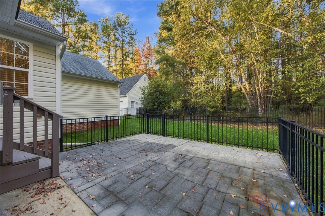 Rear stone-paver patio featuring a black metal perimeter fence, siding exterior, and wood-finish steps