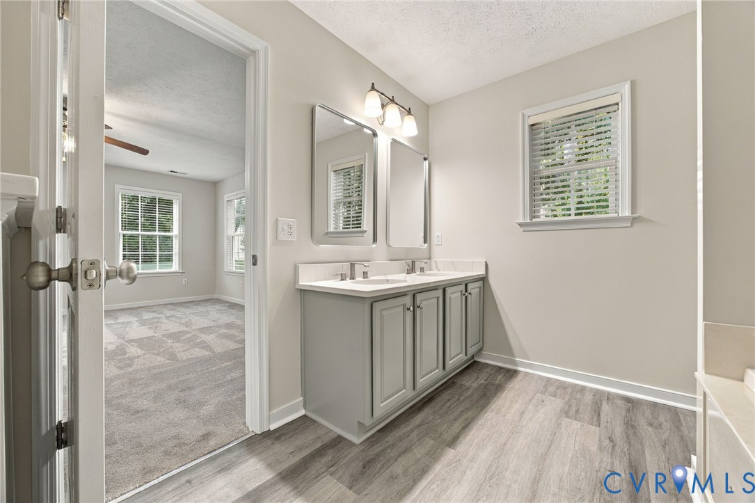 Double-sink vanity with neutral-toned cabinetry, solid-surface countertop, dual rectangular mirrors, and three-bulb vanity lighting, finished with wood-finish flooring