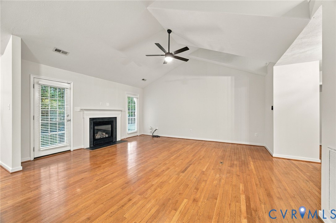 Vaulted ceilings, wood-finish flooring, fireplace with a mantel, and a ceiling fan