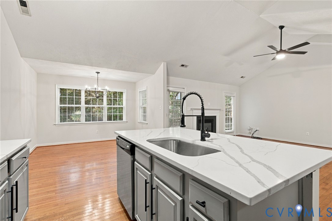 Kitchen featuring a central island with a stone-look countertop, undermount stainless steel sink, matte black gooseneck faucet, wood-finish flooring, and vaulted ceilings