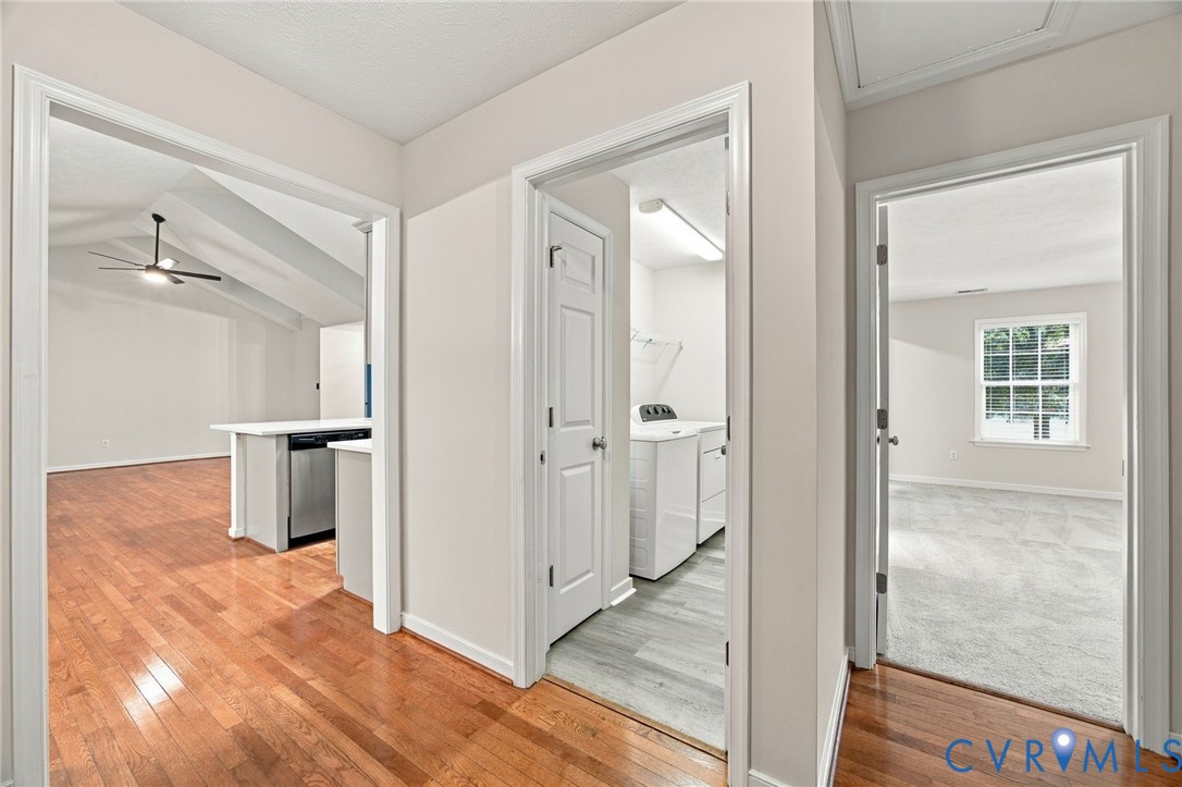 Neutral interior featuring wood-finish flooring, white paneled doors, vaulted ceilings with a mounted light fixture, and dedicated laundry space