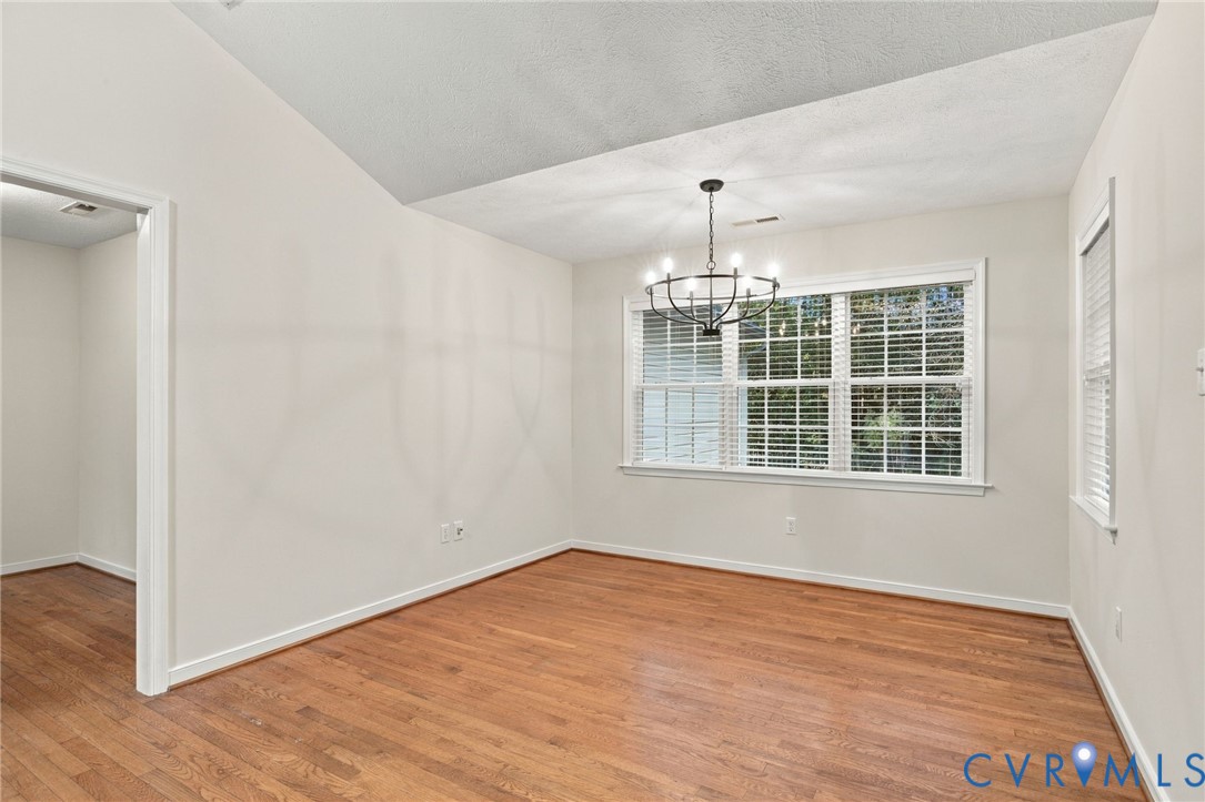 Vaulted ceiling featuring a multi-arm iron chandelier, wood-finish flooring, and multi-pane windows with horizontal blinds