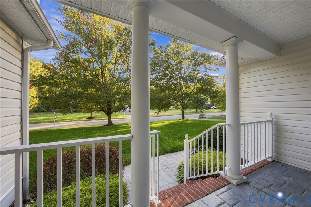 Covered front porch featuring white structural columns, stone-style pavers, a brick step detail, and white railing