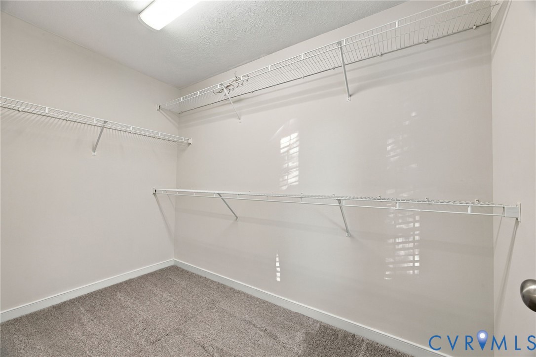 Walk-in storage space featuring neutral carpeting and multi-level white wire shelving